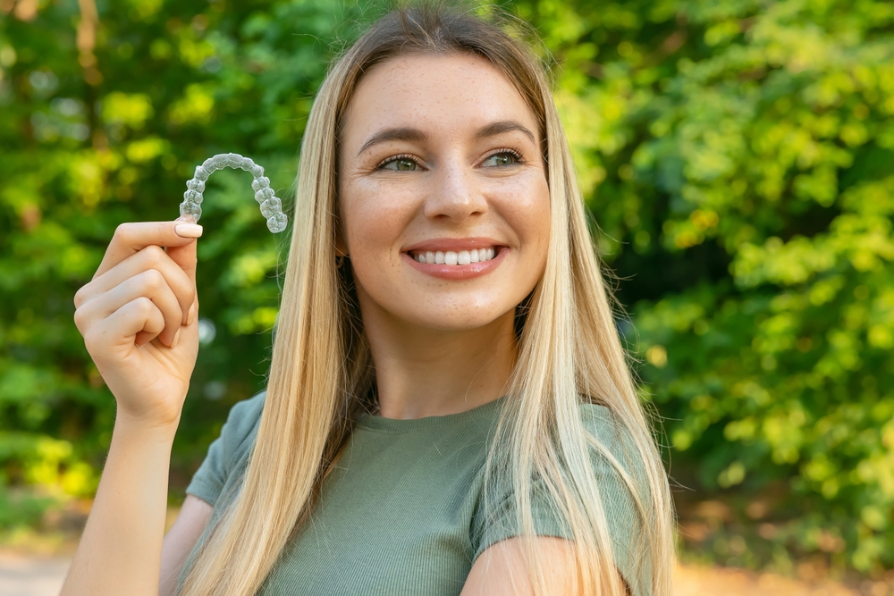 Woman holding a clear dental aligner outdoors